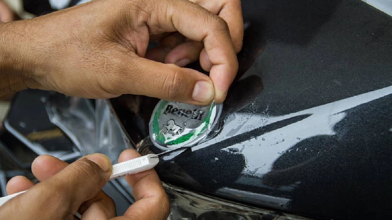 A worker cuts a clear PPF off a vehicle’s logo