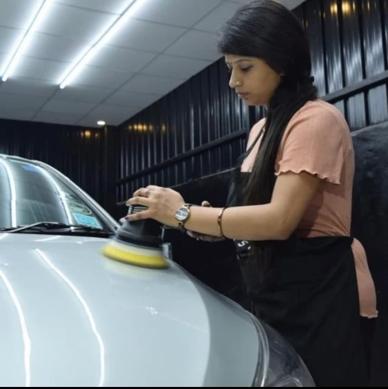 A female car detailer polishes a car inside a car detailing studio