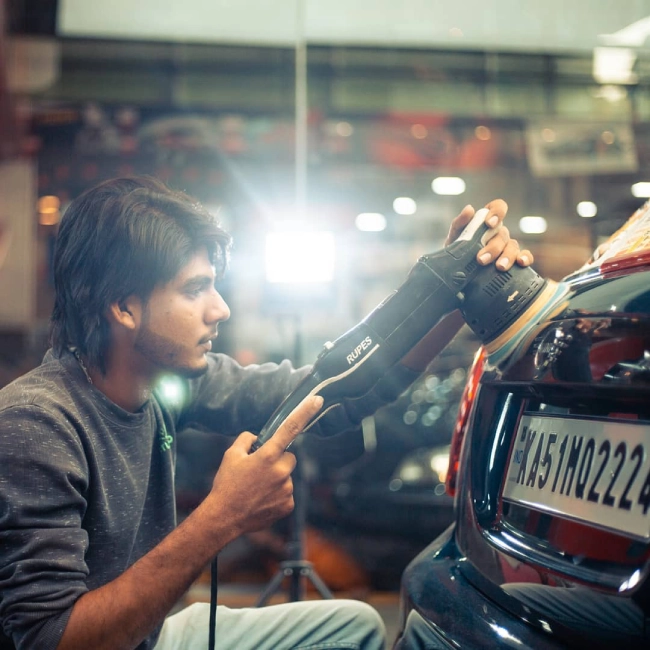 A worker polishes a black sedan inside a car detailing bay