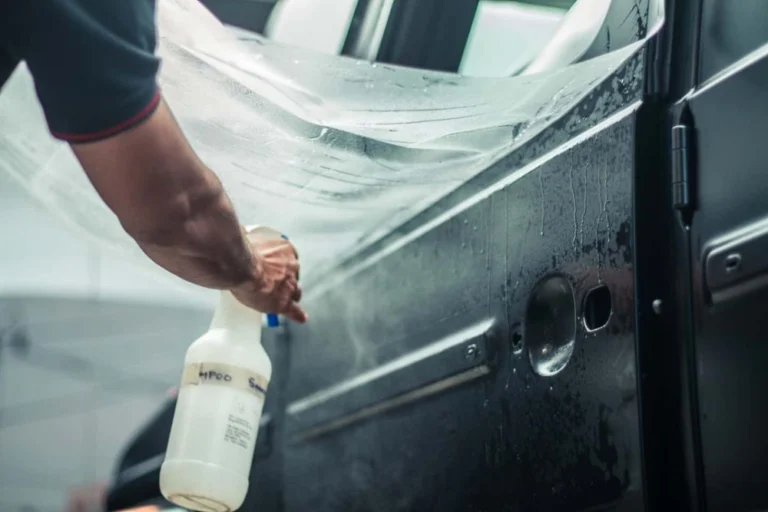 A worker sprays a solution while holding a clear PPF to apply on an SUV door