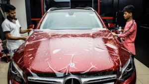 Workers install clear PPF on a maroon-coloured Mercedes sedan