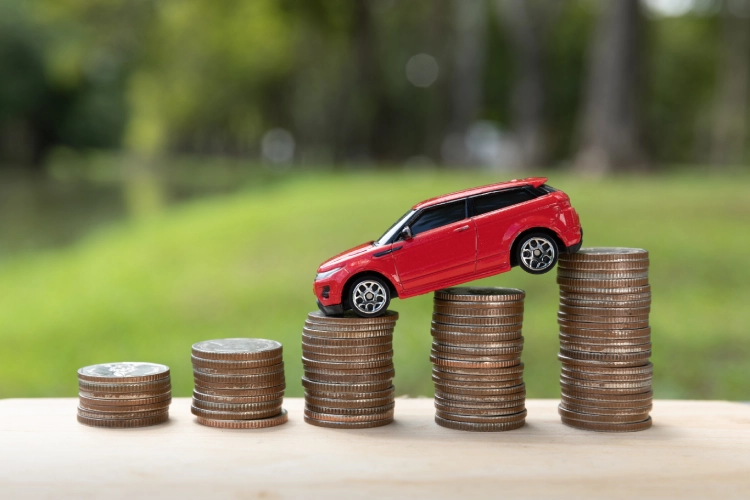 A small red toy car sits on stacks of coins arranged from shortest to tallest, symbolising rising car costs or financial growth.