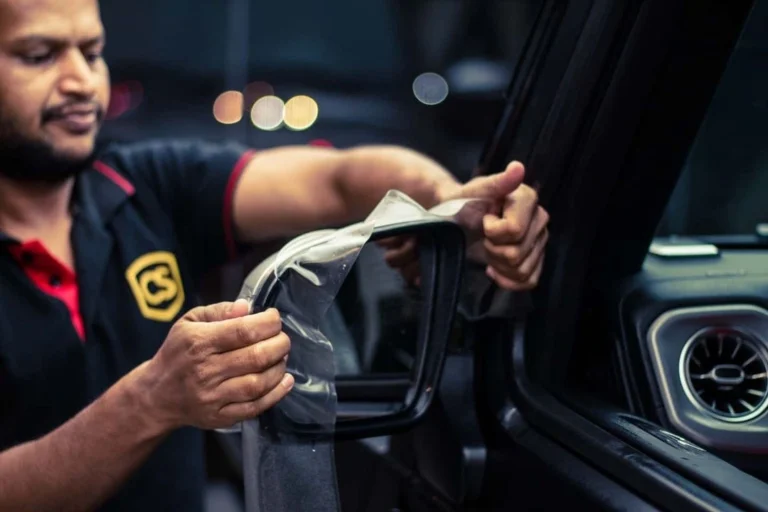 A worker installs PPF on a car’s side mirror cover