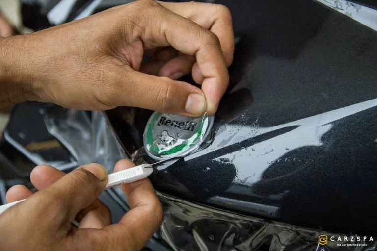 A person carefully removing the Benelli logo badge from a black car.
