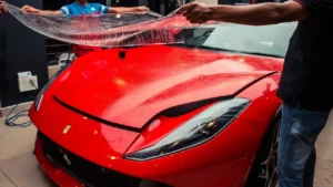 Two workers laying the clear PPF on a red Ferrari to install it.