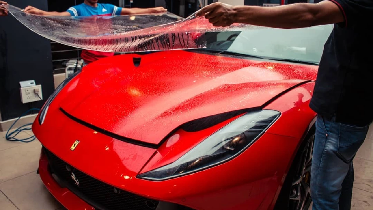 Two workers laying the clear PPF on a red Ferrari to install it.