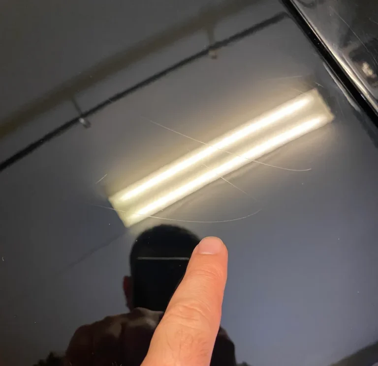 a fingernail being run on a scratched surface of a car