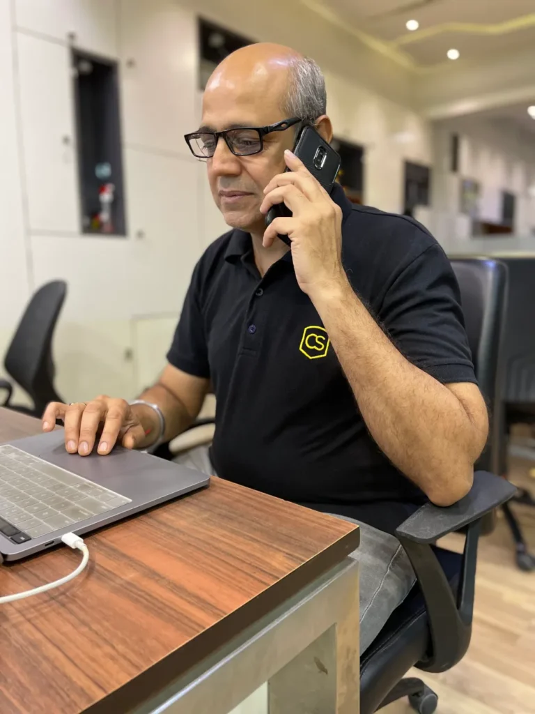 A middle-aged man on a call, while seated on a desk in his office