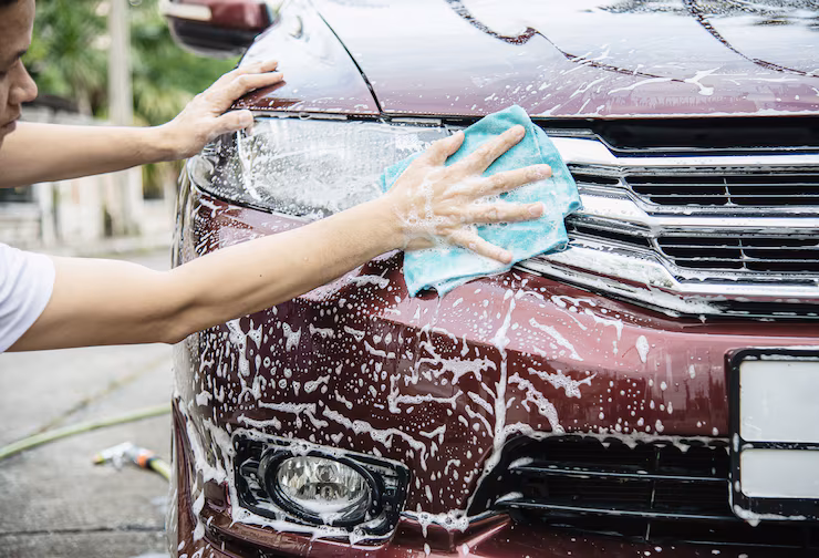 A man washing the front side of his car with soap water and cloth
